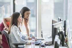 两个女人在桌子上看一系列计算机“width=