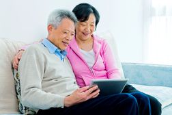 微笑的退休夫妇一起坐在沙发上看平板电脑