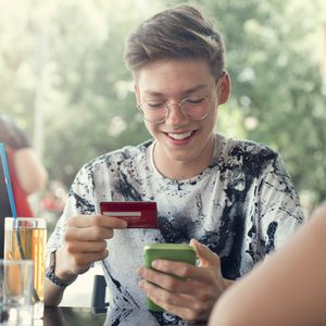 一个十几岁的男孩微笑着用他的第一张信用卡为家庭午餐付款