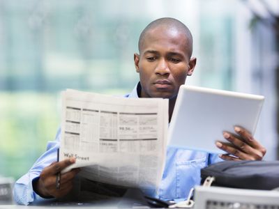 一个年轻人在查看报纸和他的平板电脑上的股票投资保证金债务