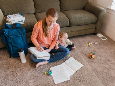 母亲在生活地板上使用纸质笔记本，婴儿旁边的婴儿