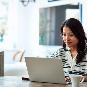 30多岁的中年女性坐在桌子旁，看着电脑，远程工作，自由职业者，小企业＂width=