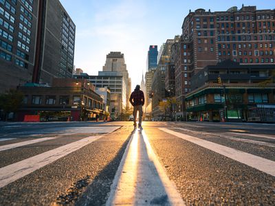 一个穿着格子夹克和软呢帽的人站在纽约一个十字路口的中央，被他们身后的阳光照亮了