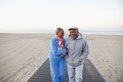 一对老年夫妇在海滩上挽臂散步，一起欢笑。