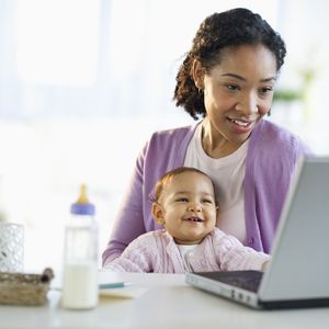 混血妇女抱着婴儿，使用笔记本电脑＂width=