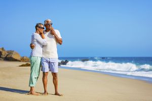 高级夫妻拥抱在海滩上,享受他们的退休计划。”width=