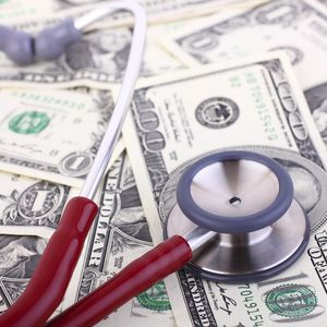 听诊器上的分散美元钞票代表医疗保健的成本。”width=