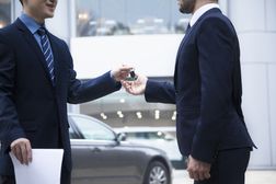 汽车推销员把一辆新车的钥匙交给一个年轻的商人