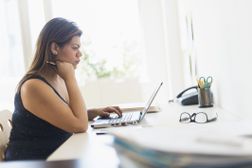 一个穿黑衬衫的女人在一个明亮的房间里用电脑工作＂width=
