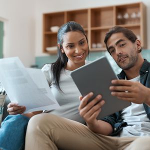 一对年轻夫妇一边在家使用平板电脑一边做文书工作的照片