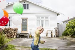 一个孩子在房子前跑步时握着气球“width=