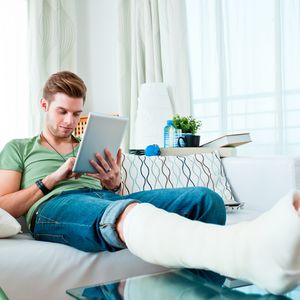 断腿的年轻人坐在沙发上看平板电脑