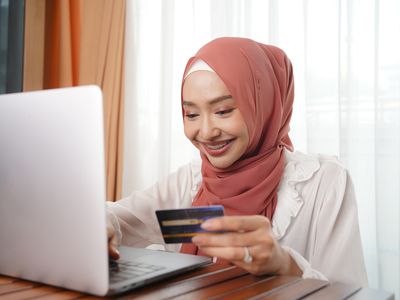 一个拿着信用卡的微笑女人使用笔记本电脑。