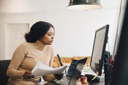 专注的女性IT专业人员在创意办公室边看电脑边拿着文件＂width=
