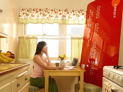 一个女人坐在一张巨大的信用卡对面＂width=