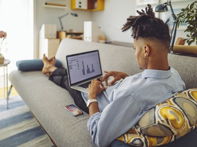年轻人在家里的笔记本电脑在他的沙发上工作