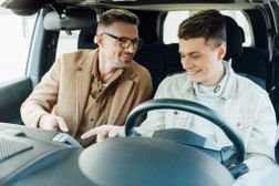 父母和青少年看一辆新车的青少年司机的座位。”width=