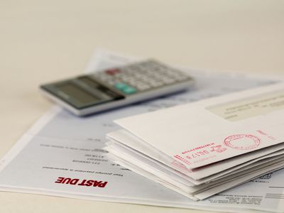 在一堆账单和计算器下面有一张盖着过期邮戳的账单＂width=