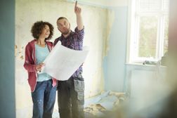 一对年轻夫妇在她的新房子刮墙的时候，抽出时间来检查他们的建筑师计划
