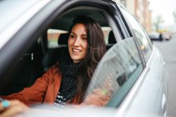 年轻女子驾驶轿车脸上带着微笑。”width=