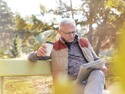 老人读报纸和咖啡在长椅上