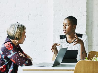 一个坐在平板电脑上的女人认真地和一个面前有笔记本电脑的女人说话