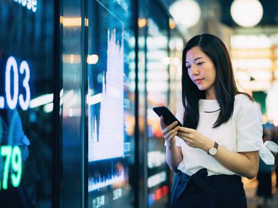 充满信心的年轻亚洲女商会检查智能手机的财务交易数据。