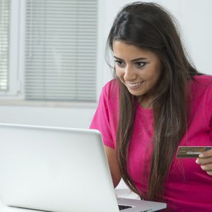 微笑的年轻女子用信用卡和笔记本电脑在网上购物。