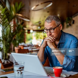 男人用笔记本电脑,坐在一家咖啡馆表看起来体贴”width=