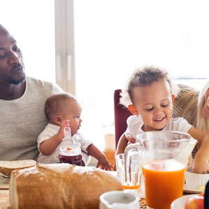 年轻漂亮的跨种族家庭与他们可爱的女儿和小宝贝的儿子一起吃早餐。”width=
