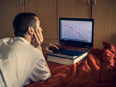 人观看在膝上型计算机屏幕上的股市崩溃在卧室