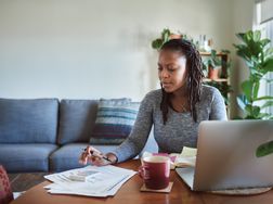 一名妇女坐在家庭桌上计算与纸和膝上型计算机的税“width=