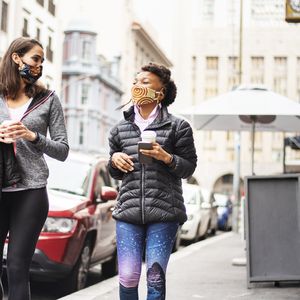 两个女人走在城市街头喝咖啡”width=