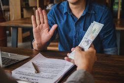 一名穿着制服的男子举起手掌，拒绝了现金的提议，他面前的桌子上放着一份合同和钢笔。＂width=