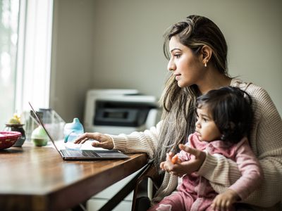 年轻的母亲带着年幼的女儿在家里用笔记本电脑处理多项任务