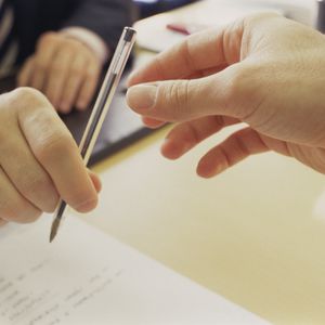 银行家将一支笔在桌子上递给申请个人贷款的人。“width=