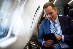 一位富有的投资者在私人飞机上看着他的平板电脑＂width=