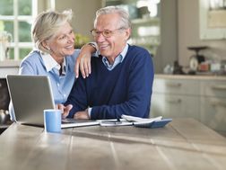 一对退休夫妇在厨房里对着笔记本电脑微笑＂width=