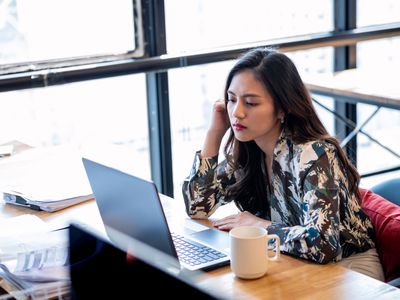 年轻的女商人喝着咖啡在办公室咨询笔记本电脑