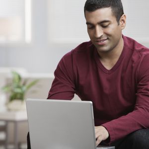 穿着红色长袖衬衫的人，坐在椅子上低头看笔记本电脑