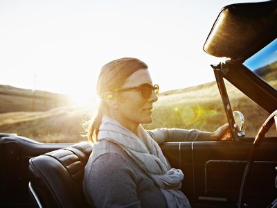 成熟的女人戴着太阳镜在日落时驾驶