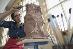 使用雕刻的工具的妇女在雕塑的作为她认为转动它进入企业