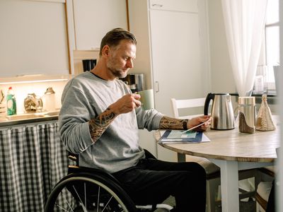 纹身成熟男人阅读邮件,拿着咖啡杯在轮椅在家里