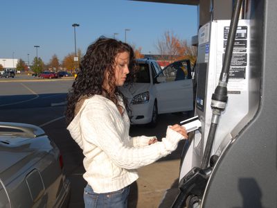 年轻女子用信用卡在泵上为汽油付款。
