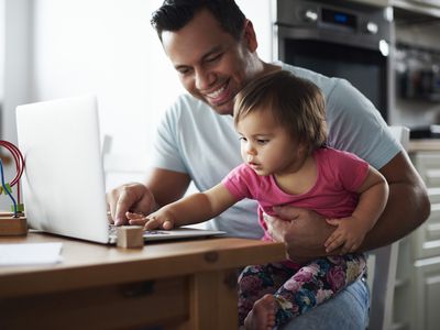 父亲和女婴在家里桌子上的笔记本电脑工作