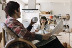 一对夫妇在厨房里讨论财务。一个人拿着报纸和一个杯子。“width=