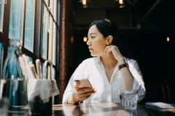 午后咖啡馆里，一名女子凝视着尘土飞扬的窗外，休息一下手中握着的智能手机。