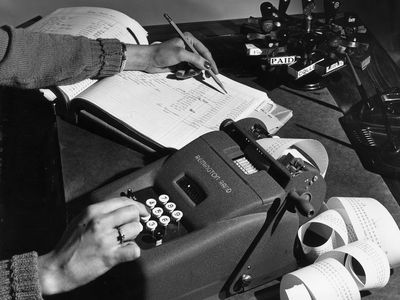 一张老照片，一个女人正在用一个大计算器在总账上写数字