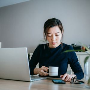 年轻女子一边喝咖啡一边用笔记本电脑和手机工作