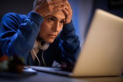 一个女人震惊地凝视着笔记本电脑屏幕时，将双手握在额头上：她的僵尸债务已经返回“width=
